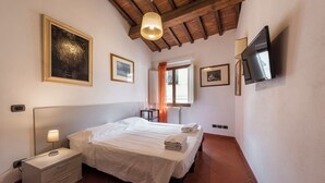 Een slaapkamer met een bed, nachtkastje, lamp en een aan de muur bevestigde televisie.