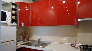 A kitchen with red cabinets, a stainless steel sink, a microwave, and a gas stove. - Veneto Apartment (Lucca)