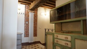 Un couloir étroit aux murs en briques apparentes, avec un radiateur et un sol à carreaux.