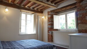 Une chambre à coucher avec un lit, deux fenêtres et des murs en briques apparentes.