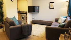 Sala de estar con sofá, televisión, lavadora y un reloj en la pared.