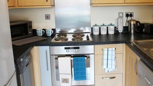 Una cocina moderna con armarios de madera, una campana extractora de acero inoxidable, un microondas, una estufa, un horno y un lavavajillas. También hay tazas de café y un hervidor en la encimera.