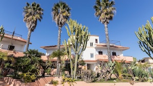 A multi-story building with a white facade and red-tiled roof, surrounded by palm trees and cacti. - Residence Esmeraldo (Ricadi)