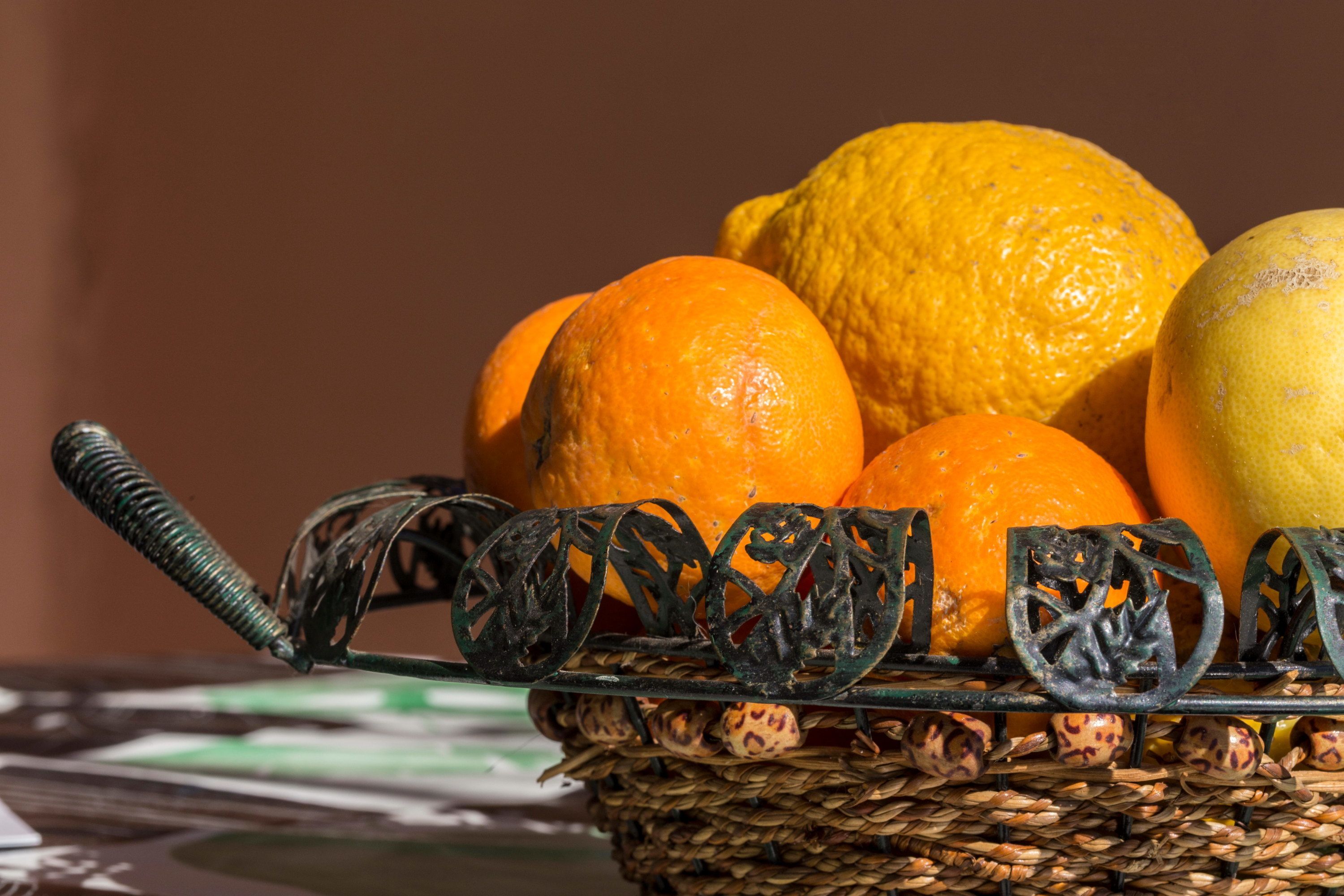 Un panier en osier contenant des oranges et un citron, posé sur une table.
