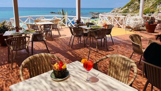 An outdoor dining area with tables and chairs, overlooking a beach and the sea. - Residence Esmeraldo (Ricadi)