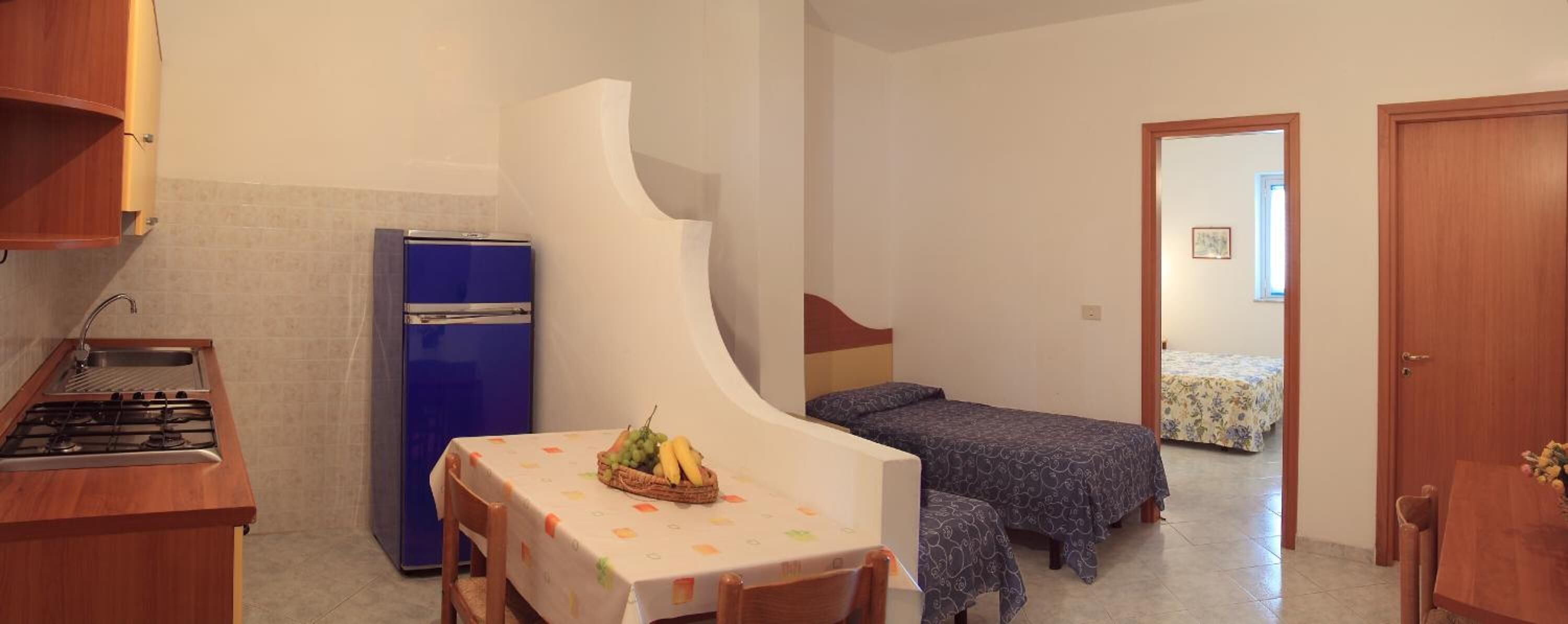 Una habitación compacta con kitchenette, una cama y una pequeña mesa con fruta.