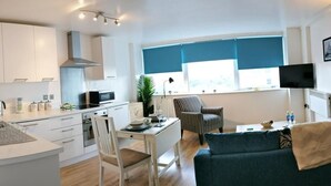Een moderne keuken met witte kasten, een eethoek met een gestreepte stoel, een blauwe bank en een aan de muur bevestigde televisie.