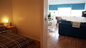 Een slaapkamer met een bed en nachtkastje, een zithoek met een tafel en stoelen, en een woongedeelte met een bank en televisie.