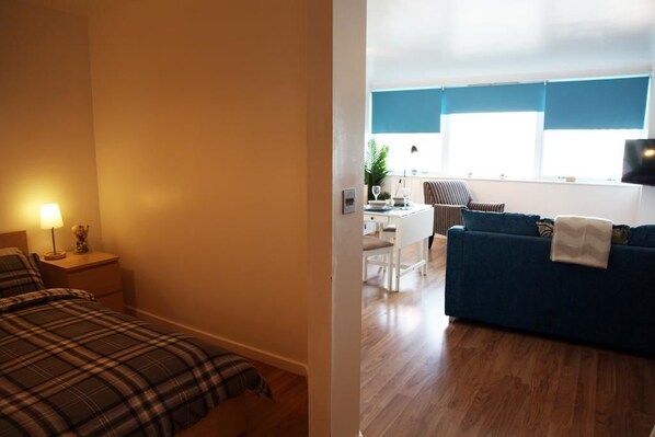 Une chambre avec un lit et une table de chevet, un coin repas avec une table et des chaises, et un salon avec un canapé et un téléviseur.