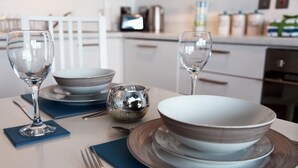 Een eettafel gedekt met helder glaswerk, borden en een decoratieve schaal, met een moderne keuken op de achtergrond.