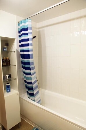 Une salle de bain avec une baignoire, un rideau de douche à rayures et une étagère contenant des articles de toilette.