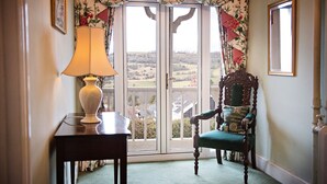 A room with a view through a glass door, a wooden chair, a table with a lamp, and a mirror on the wall. - Cleeve Hill Hotel (Cheltenham)