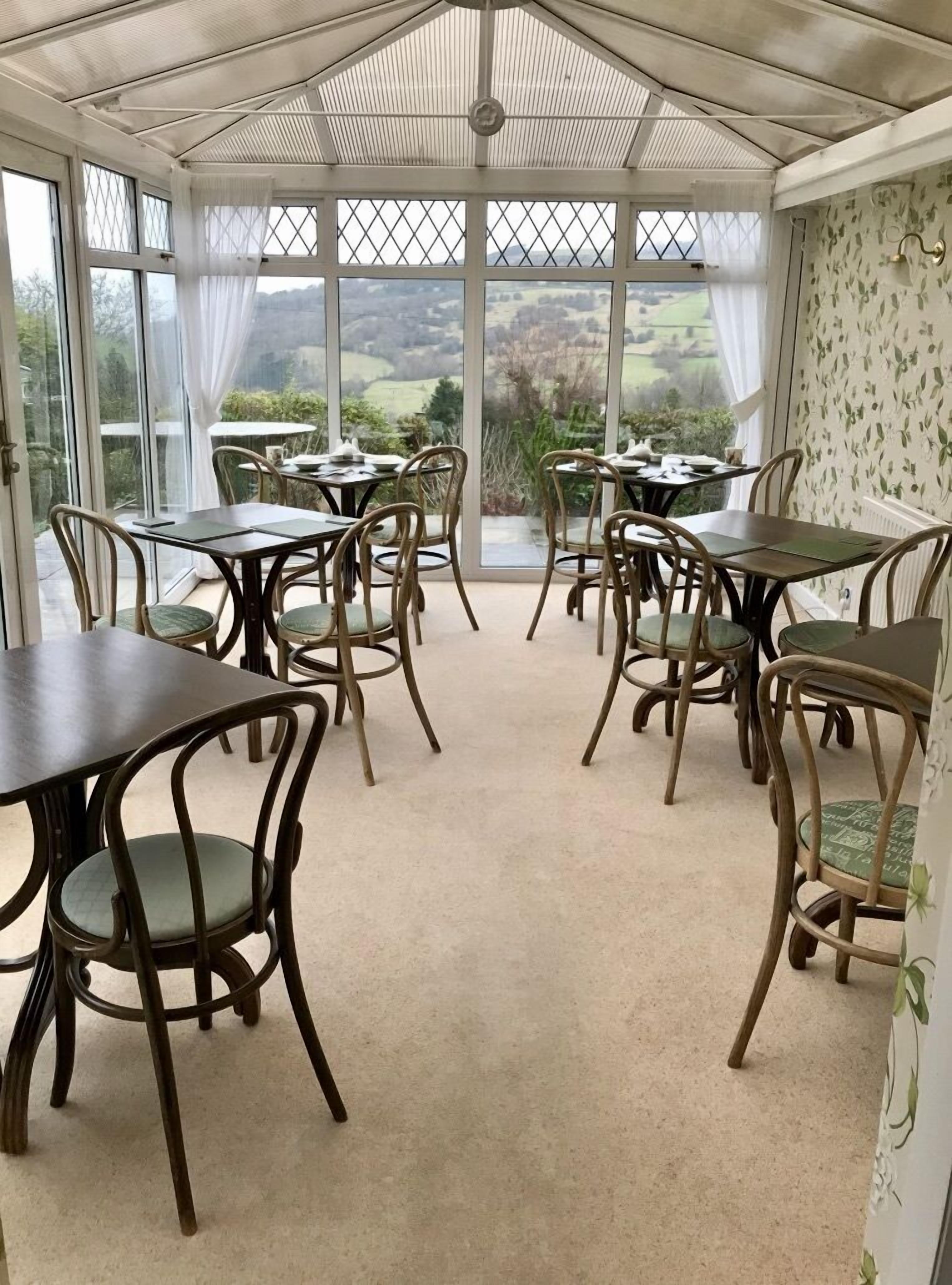 A conservatory with tables and chairs, large windows, and a view of the countryside.
