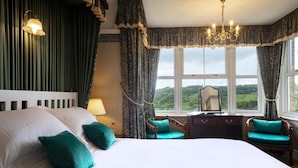 A bedroom with a large bed, two chairs, a dresser, and a view of the countryside. - Cleeve Hill Hotel (Cheltenham)