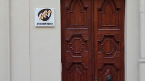 Una puerta doble de madera con un diseño decorativo, un letrero encima que dice "Art Guest House" y el número "88" en la pared a la derecha.