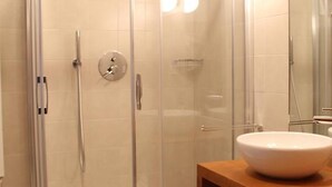 Un baño moderno con ducha de vidrio, tocador de madera con un lavamanos grande y suelo de baldosas.