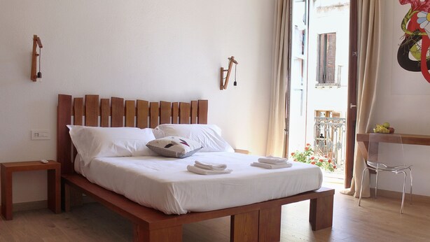 Una cama bien hecha con ropa blanca, un cabecero de madera y una mesita de noche con una lámpara.