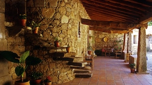 A stone-walled patio with terracotta tiles, potted plants, and rustic wooden furniture. - Finca El Cabezo (Villamiel)