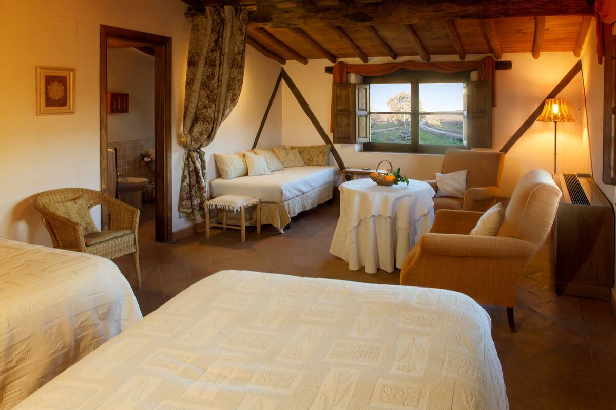 A cozy room with two beds, a sofa, a dining table, and a window with a view.