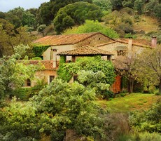 Una casa de piedra con tejado de tejas, rodeada de abundante vegetación y árboles.