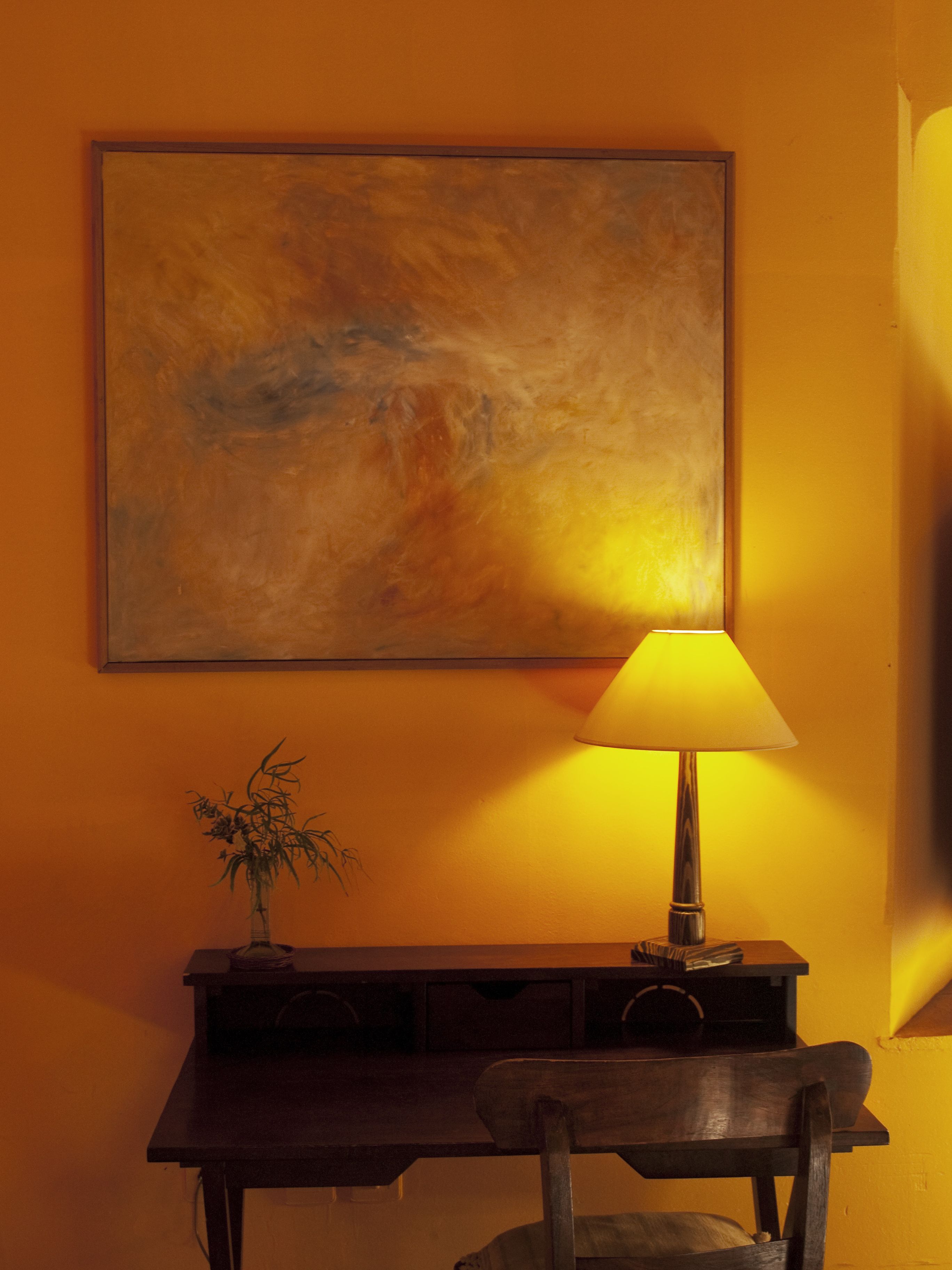 Une pièce avec un bureau, une lampe et un tableau au mur.