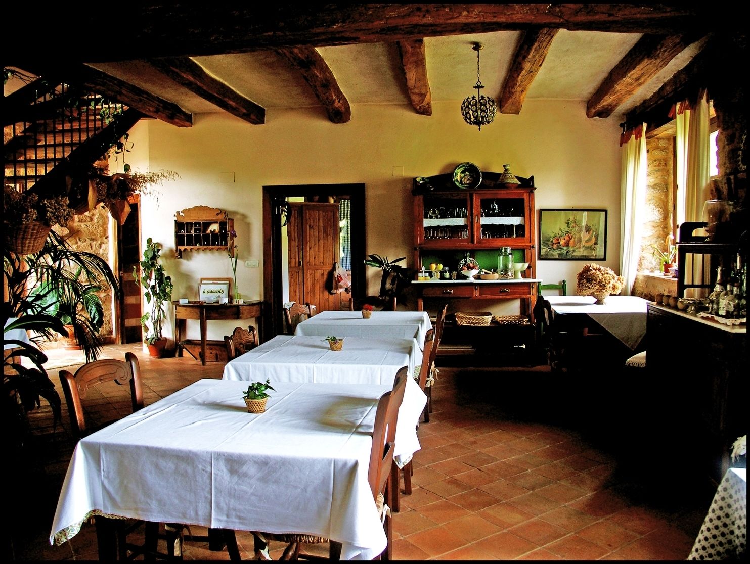 A dining area with multiple tables set for a meal, wooden beams on the ceiling, and a rustic ambiance.