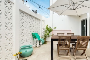 A patio with a wooden table and chairs, white lattice wall, and potted plants. - TROPICALIA by DW (San Juan)
