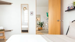 A modern bedroom with a large bed, a wooden door, a mirror, and a small desk with a chair. - TROPICALIA by DW (San Juan)