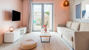 A modern living room with a flat-screen TV, a white console table, a beige sofa, a wooden coffee table with a vase of flowers, and a large sliding glass door leading to an outdoor area. - TROPICALIA by DW (San Juan)