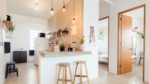A modern kitchen with wooden stools, a refrigerator, and a countertop with various kitchen items. - TROPICALIA by DW (San Juan)