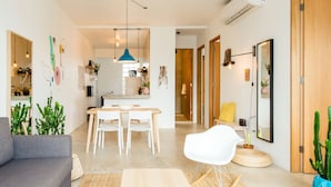 A modern living room with a grey sofa, a white chair, a dining table with chairs, a blue pendant light, and a wooden door. - TROPICALIA by DW (San Juan)