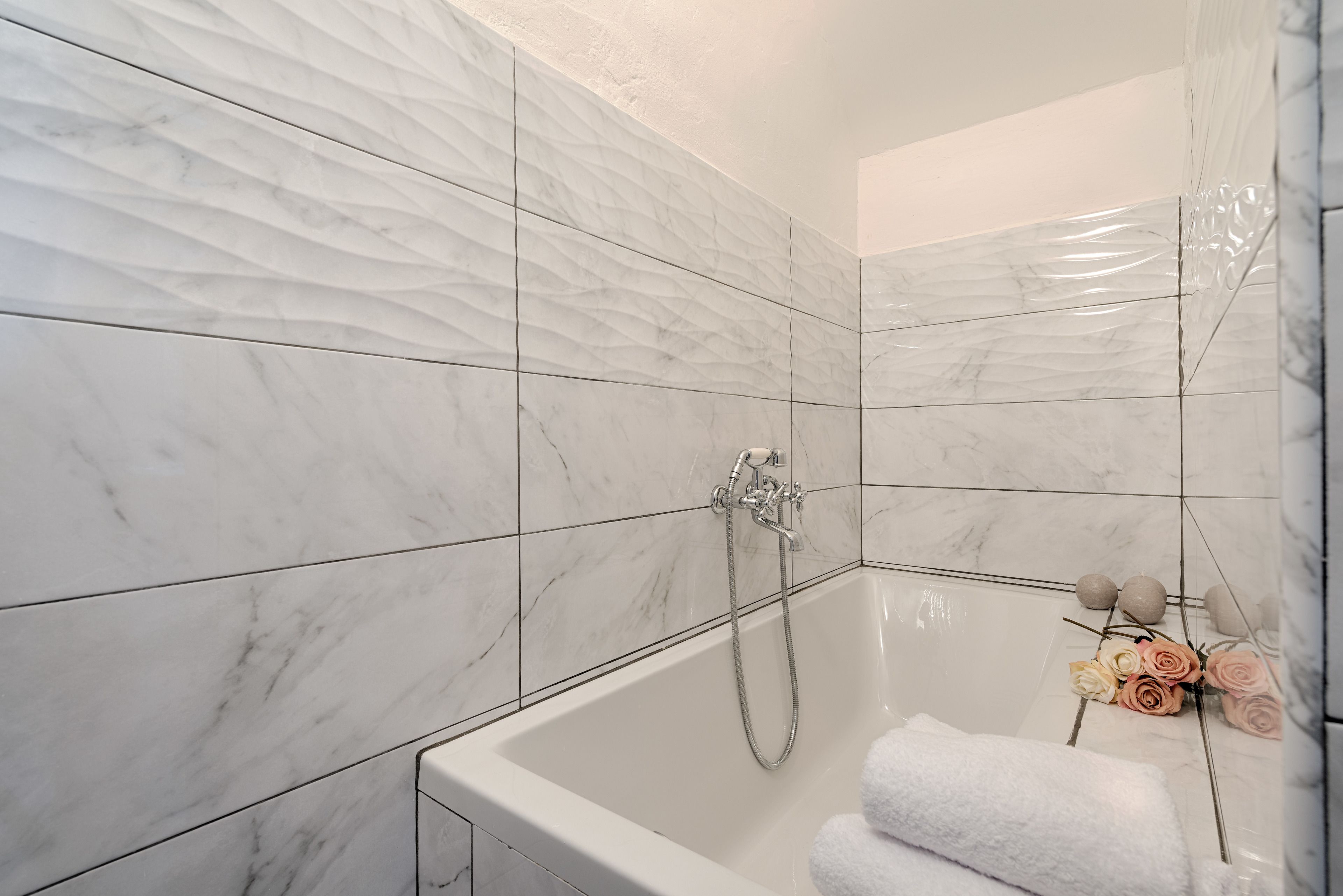 A modern bathroom with white marble tiles, a bathtub, and a shower.