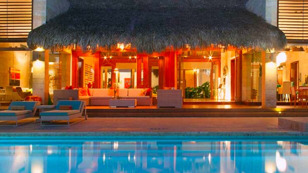 A poolside area with lounge chairs and a thatched-roof structure. - Villa Perla by Unlimted Luxury Villas (La Romana)