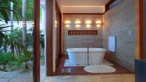 A modern bathroom with a freestanding bathtub, recessed lighting, and a stone wall. - Villa Perla by Unlimted Luxury Villas (La Romana)