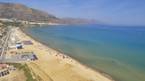 A coastal beach with a parking lot, beach umbrellas, and a mountainous backdrop. - Riva Sea Apartments (Castellammare del Golfo)