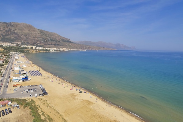 A coastal beach with a parking lot, beach umbrellas, and a mountainous backdrop.