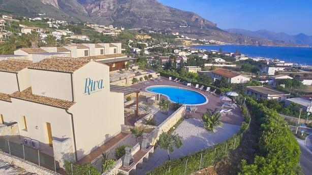 A resort with a swimming pool, lounge chairs, and a view of the sea and mountains. - Riva Sea Apartments (Castellammare del Golfo)