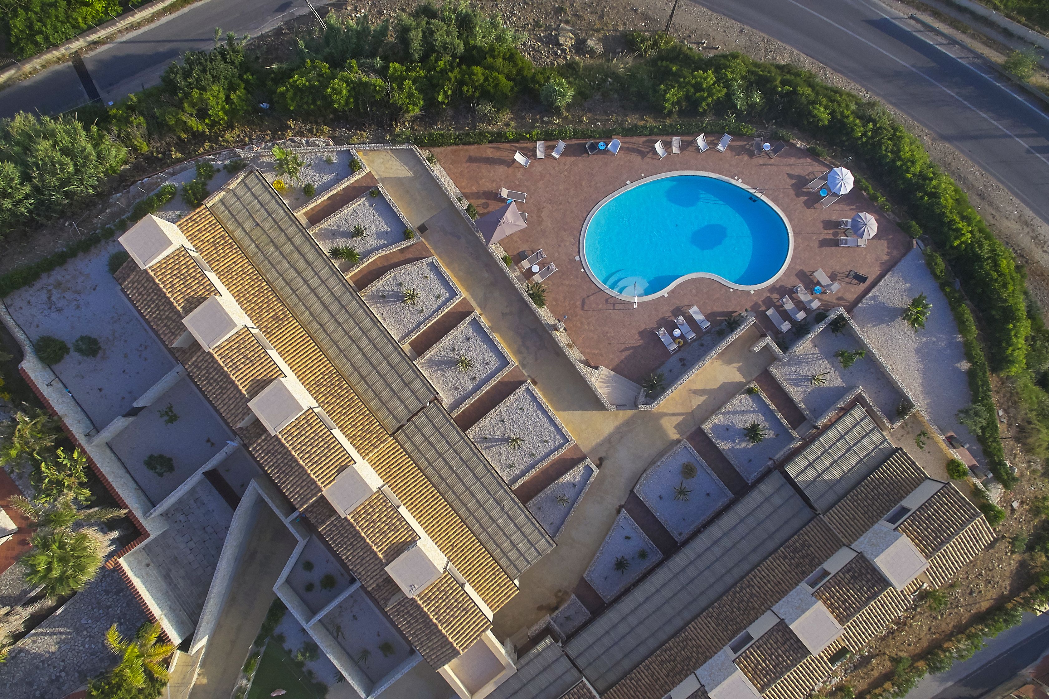 An aerial view of a hotel with a swimming pool, sun loungers, and a landscaped garden.