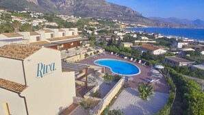 A residential area with a swimming pool surrounded by lounge chairs and umbrellas, indicating a resort or vacation setting. - Riva Sea Apartments (Castellammare del Golfo)