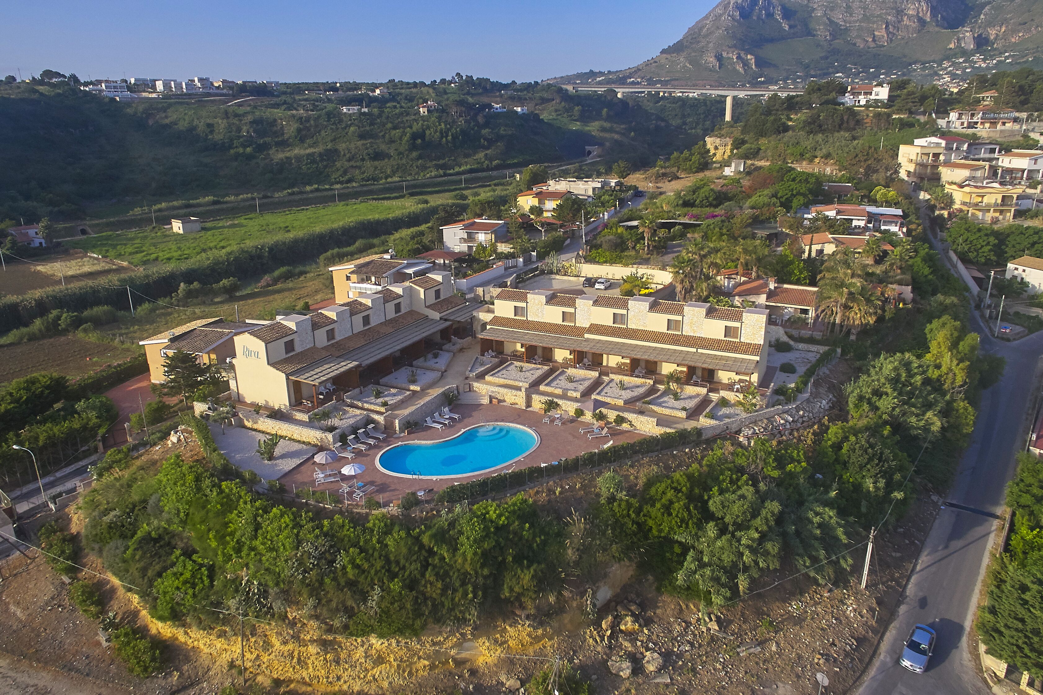 An aerial view of a resort with a swimming pool, multiple buildings, and surrounding greenery.