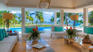 A spacious living area with a view of a pool and palm trees. - Casa Feliz by Unlimited Luxury Villas (La Romana)