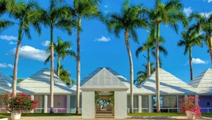 A resort with multiple white-roofed buildings, surrounded by palm trees, and featuring a central open pavilion. - Casa Feliz by Unlimited Luxury Villas (La Romana)