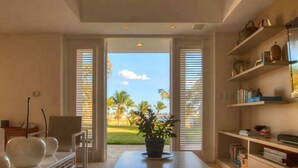 A room with a large window, a potted plant, a chair, and a bookshelf. - Casa Feliz by Unlimited Luxury Villas (La Romana)