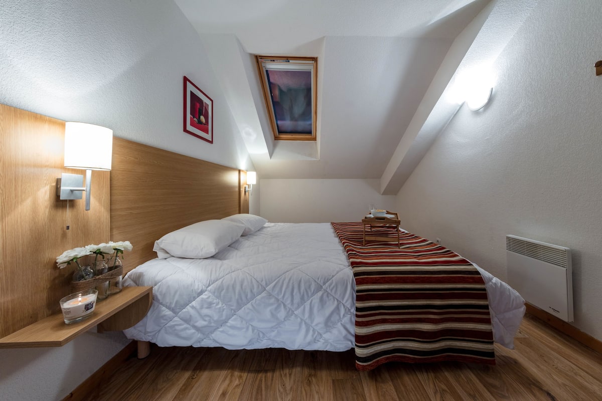 Ein Schlafzimmer mit Bett, Nachttisch, Lampe und einem Fenster mit Blick.