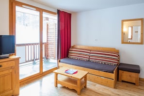 A cozy room with a wooden sofa, a small wooden table, a television on a cabinet, and a sliding glass door leading to an outdoor area. - Noemys Les Balcons de Bois Méan (Les Orres)