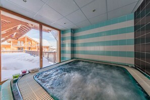A hot tub with a view of a wooden cabin and snowy landscape.