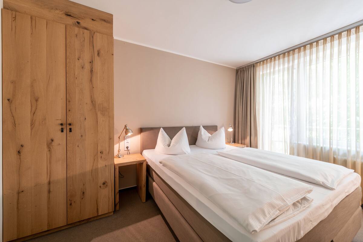 Ein Schlafzimmer mit großem Holzschrank, einem Bett mit weißer Bettwäsche und einem Nachttisch mit Lampen.