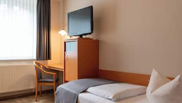 Ein Hotelzimmer mit Bett, Schreibtisch, Stuhl, Fernseher auf einem Standfuß und einem fenster mit Vorhängen.