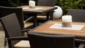 Un patio con muebles de mimbre y una mesa de madera, con dos candelabros y velas blancas.