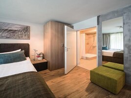 Habitación de hotel moderna con una cama grande, una mesita de noche, un armario y un baño visible a través de una puerta abierta.